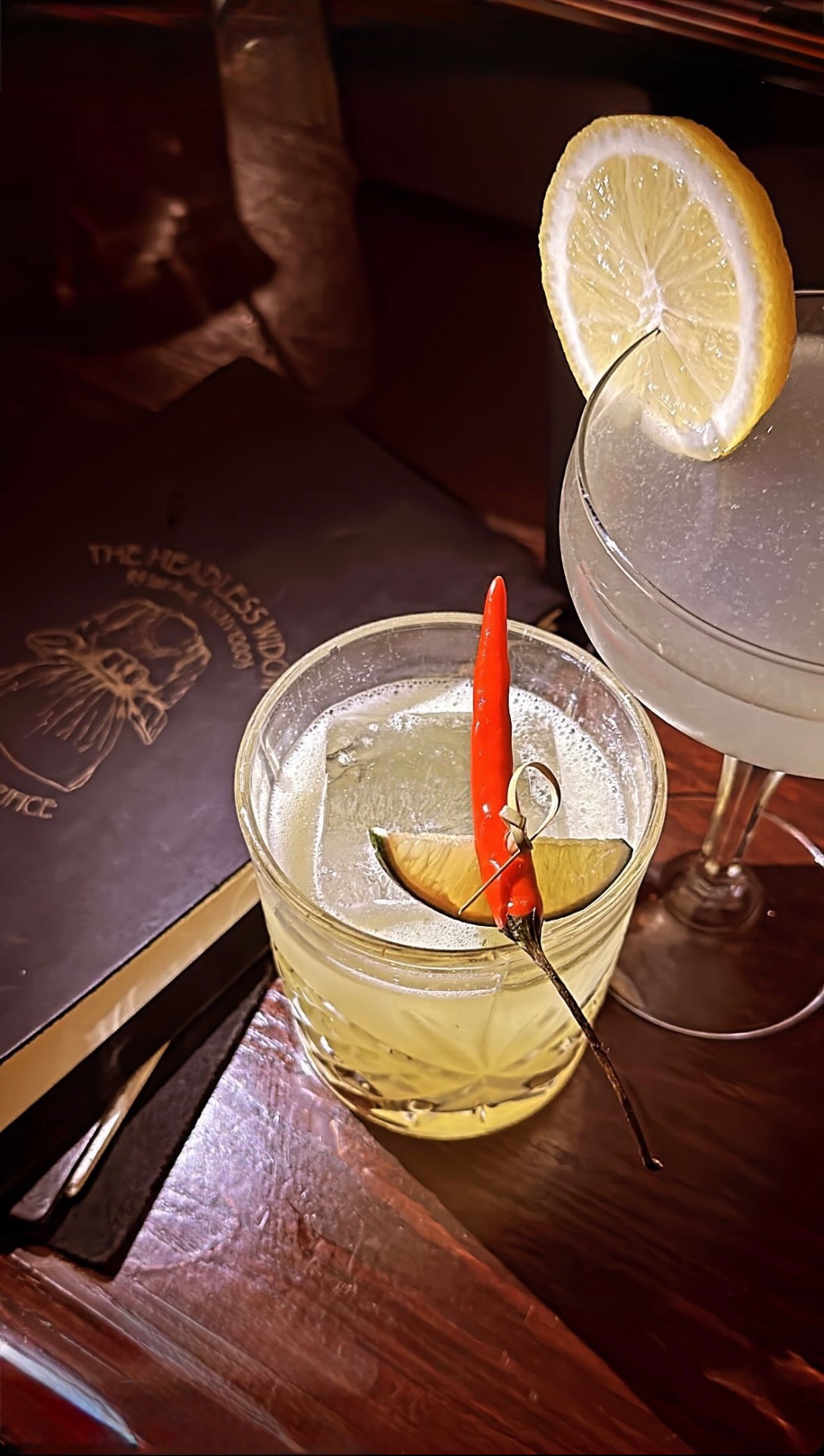 A chili-and-lime garnished cocktail beside a frosted coupe at Headless Widow