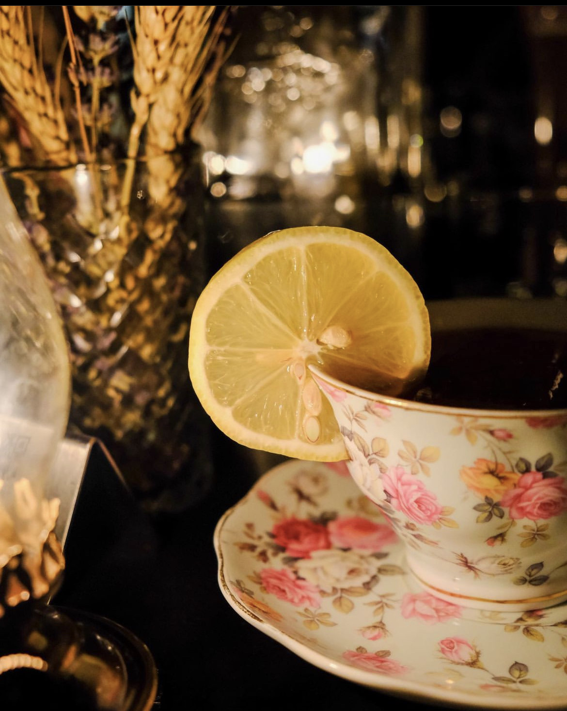 A dark cocktail served in a floral vintage teacup with a lemon wheel